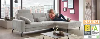 Großes graues Ecksofa im modernen Wohnzimmer mit RAL Gütezeichen Möbelqualität. Die Frau liest entspannt auf dem Sofa, das mit Kissen und Couchtisch mit Deko ausgestattet ist.